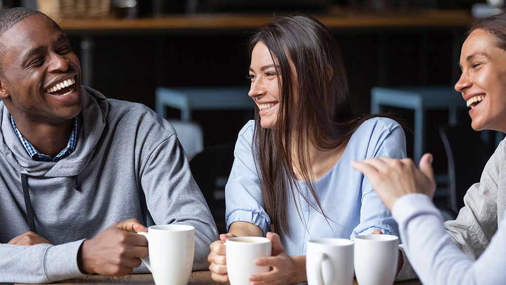 Three smiling people enjoying coffee.