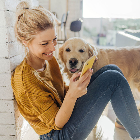 Woman using smartphone while happy dog looks on.