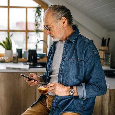 Man holding coffee looking at phone at home.