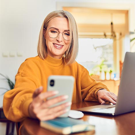 Woman looking at phone using laptop.